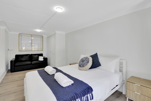 A modern bedroom with a large bed, a black sofa, a wooden nightstand, and a mirror on the wall. - The location couldn’t be more convenient (Amity)
