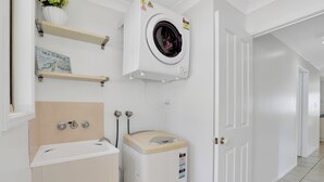 A laundry room with a washing machine, a sink, and a shelf with a sign.
