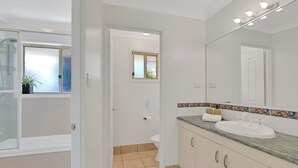 A modern bathroom with a large mirror, a sink, and a shower area. - The location couldn’t be more convenient (Amity)