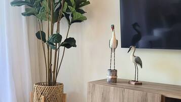 A room with a wooden floor, a woven plant stand, a wooden console table, and a wall-mounted flat-screen TV.