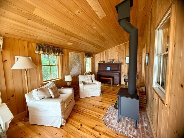 A wooden cabin interior with a fireplace, two white sofas, and a piano.