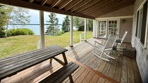 A wooden deck with a picnic table and white rocking chairs, overlooking a lake and trees.