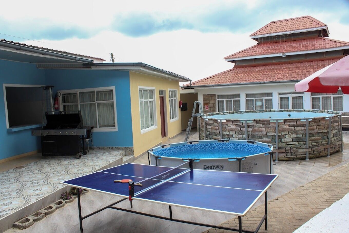 An outdoor area with a ping pong table, a barbecue grill, and a swimming pool.