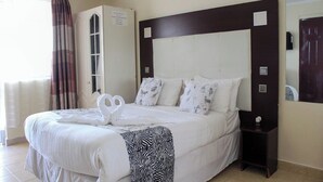 Una habitación de hotel con una cama grande, un armario, un espejo y una ventana con cortinas.