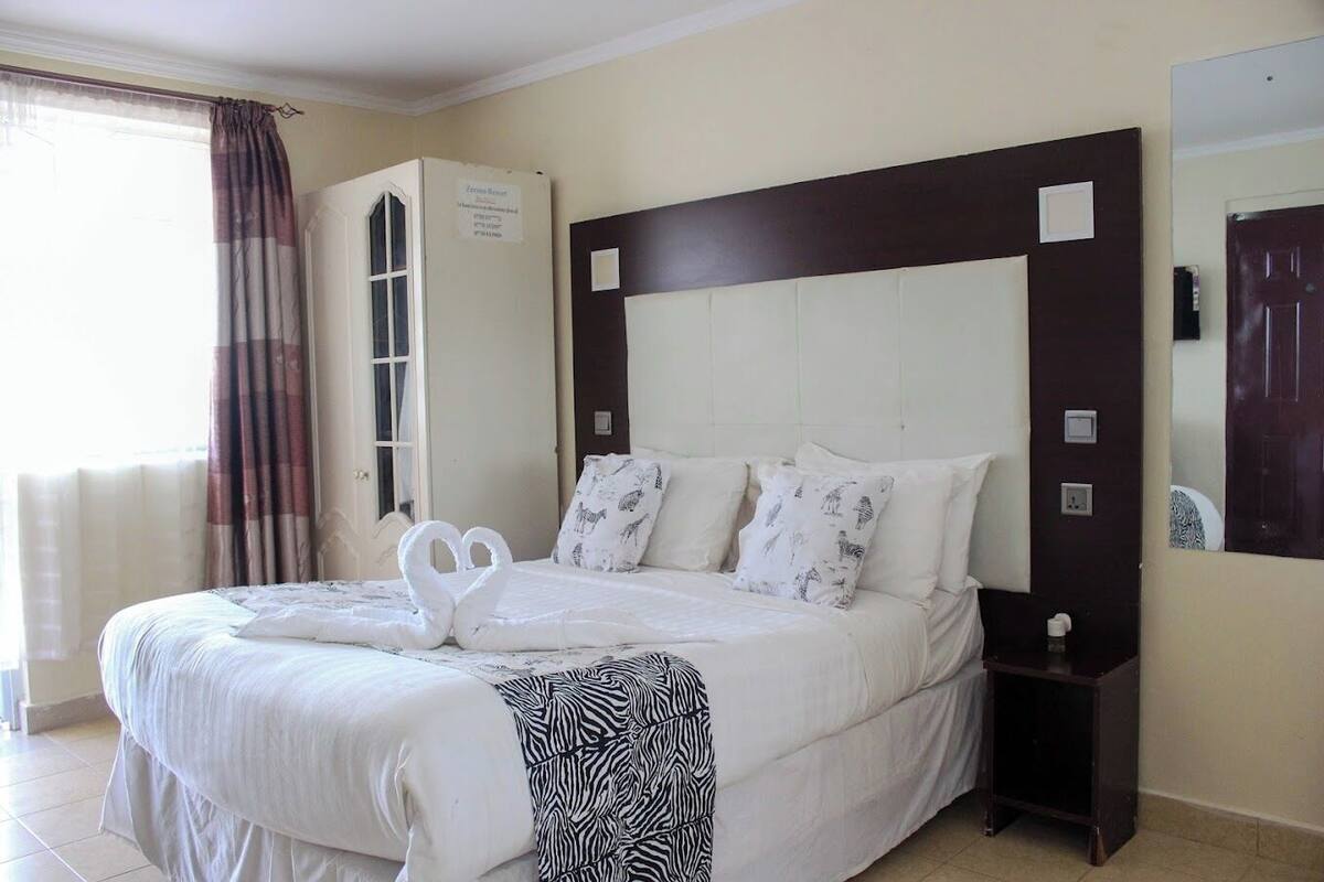 A hotel room with a large bed, a wardrobe, a mirror, and a window with curtains.