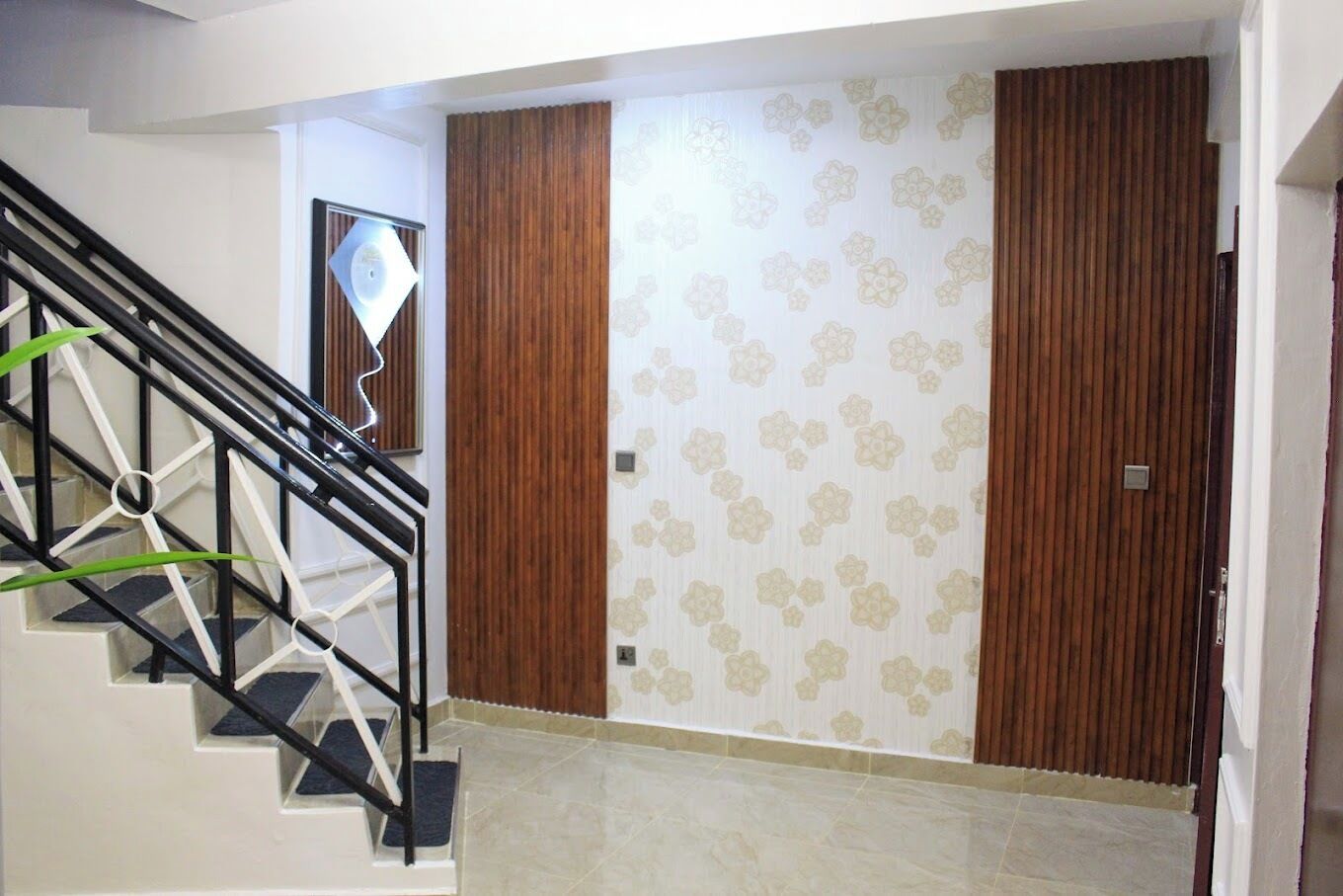 A staircase with a black metal railing leading to a room with wooden doors and patterned wallpaper.