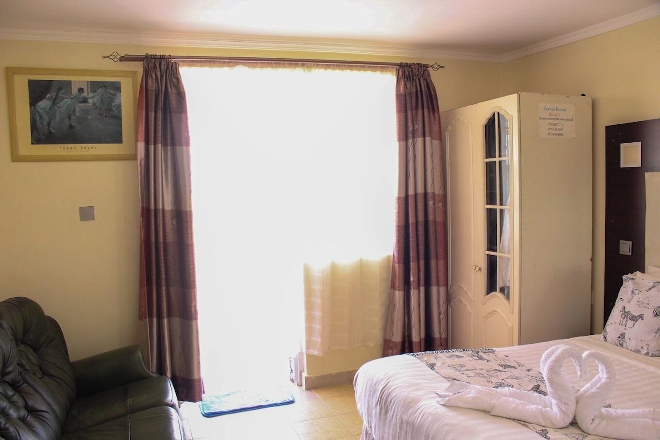 A hotel room with a bed, a chair, a door, and a window with curtains.