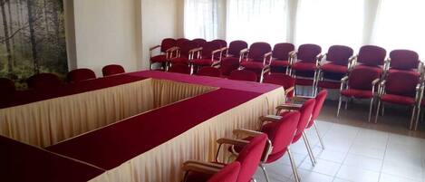 Ein Konferenzraum mit einem langen Tisch, roten Stühlen, großen Fenstern und einem Gemälde an der Wand.