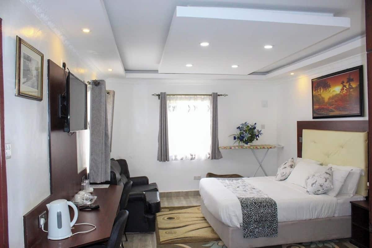 A hotel room with a bed, desk, chair, and a small table with a kettle.