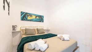 A bedroom with a bed, pillows, a blanket, and a painting on the wall.