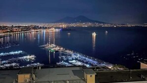 A nighttime view of a coastal city with a prominent bridge, a marina, and a mountain in the background.
