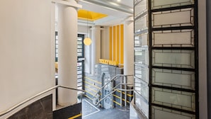 Um interior moderno com escada, área de recepção e elevador de vidro.