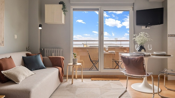 Uma sala de estar com sofá, uma mesa de jantar com cadeiras, TV na parede e varanda com vista para o mar.