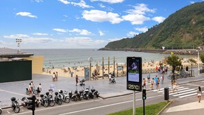 Vista à beira-mar com uma estrada, scooters estacionados e uma faixa de pedestres.