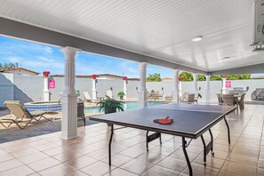 An outdoor pool area with a ping pong table, lounge chairs, and a covered seating area.