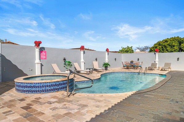 Piscina com espreguiçadeiras e hidromassagem, cercada por um muro baixo e plantas em vasos.
