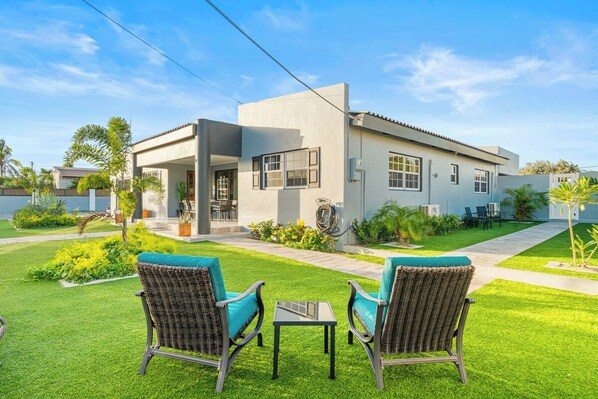 A modern house with a patio area featuring two wicker chairs and a small table. - Incredible 4 BR Home with Private Pool Near Ocean (Pos Chiquito)