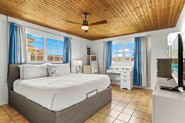 A bedroom with a bed, a desk, a TV, and a ceiling fan.