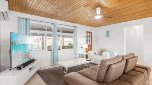 Een woonkamer met een houten plafond, een witte bank, een bruine leren divan, een glazen salontafel en een flatscreen televisie.