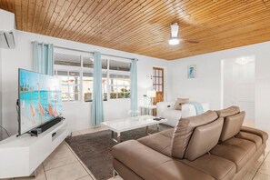 A living room with a wooden ceiling, a white sofa, a brown leather couch, a glass coffee table, and a flat-screen TV. - Incredible 4 BR Home with Private Pool Near Ocean (Pos Chiquito)