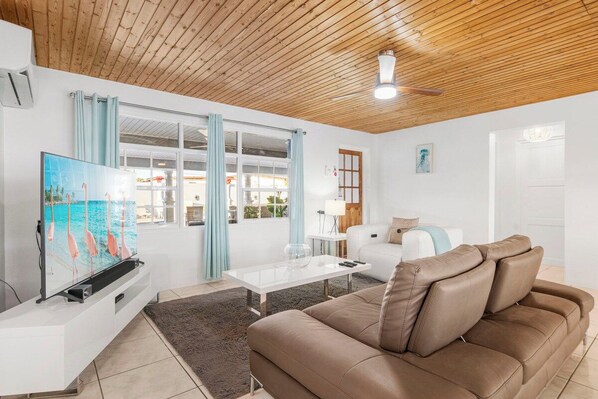 A living room with a wooden ceiling, a white sofa, a brown leather couch, a glass coffee table, and a flat-screen TV. - Incredible 4 BR Home with Private Pool Near Ocean (Pos Chiquito)