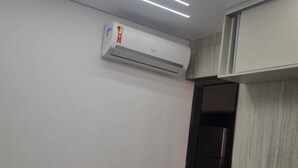 Ein Zimmer mit Bett, Klimaanlage, Tür und einer Wandablage.