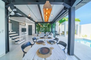 A modern dining area with a pool view, featuring a long table set for six, black chairs, and a ceiling with industrial-style pendant lights. - Exclusive Villa with Breathtaking Views, Bali Villa 2159 (Bali)