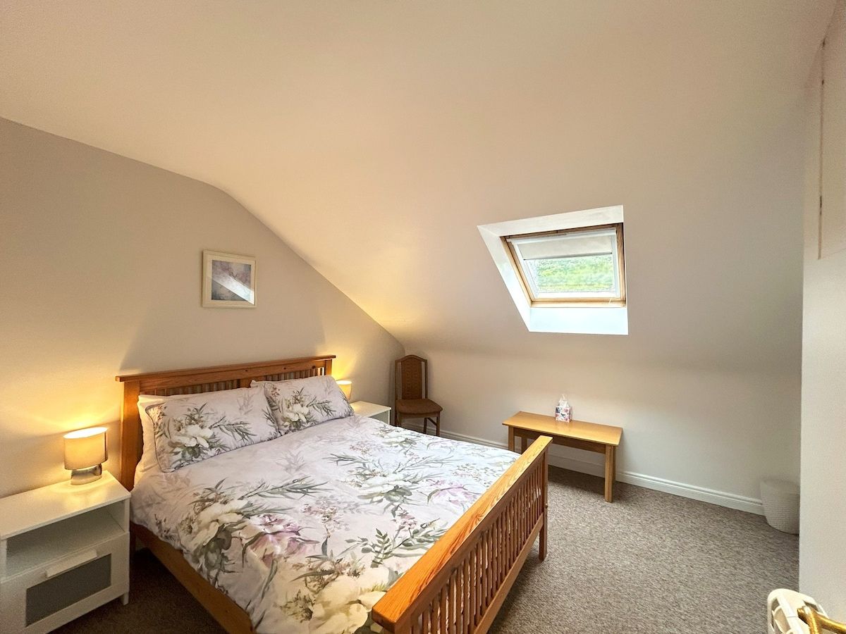 Ein Schlafzimmer mit einem Bett, Nachttischen, einer Bank, einem Oberlicht und einem kleinen Fenster.