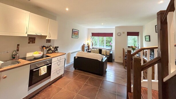 A modern kitchen with white cabinets, a built-in oven, and a dining area with a black sofa and a table.