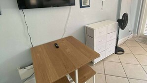 A room with a wooden table, a white cabinet, a wall-mounted TV, and a standing fan. - Charming Studio condo in excellent Daytona Beach (Daytona Beach)