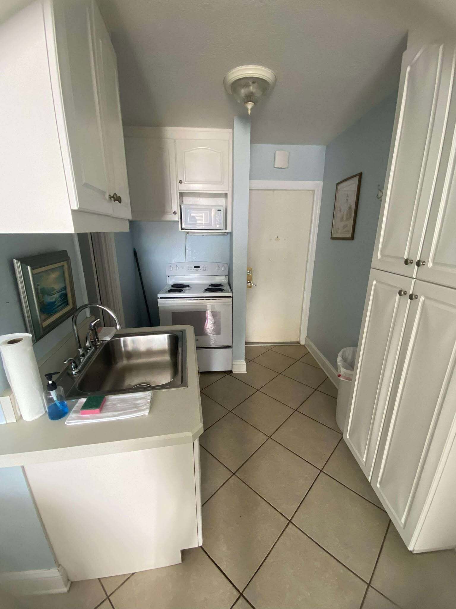 A compact kitchen with white cabinets, a stainless steel sink, a microwave, and a stove.