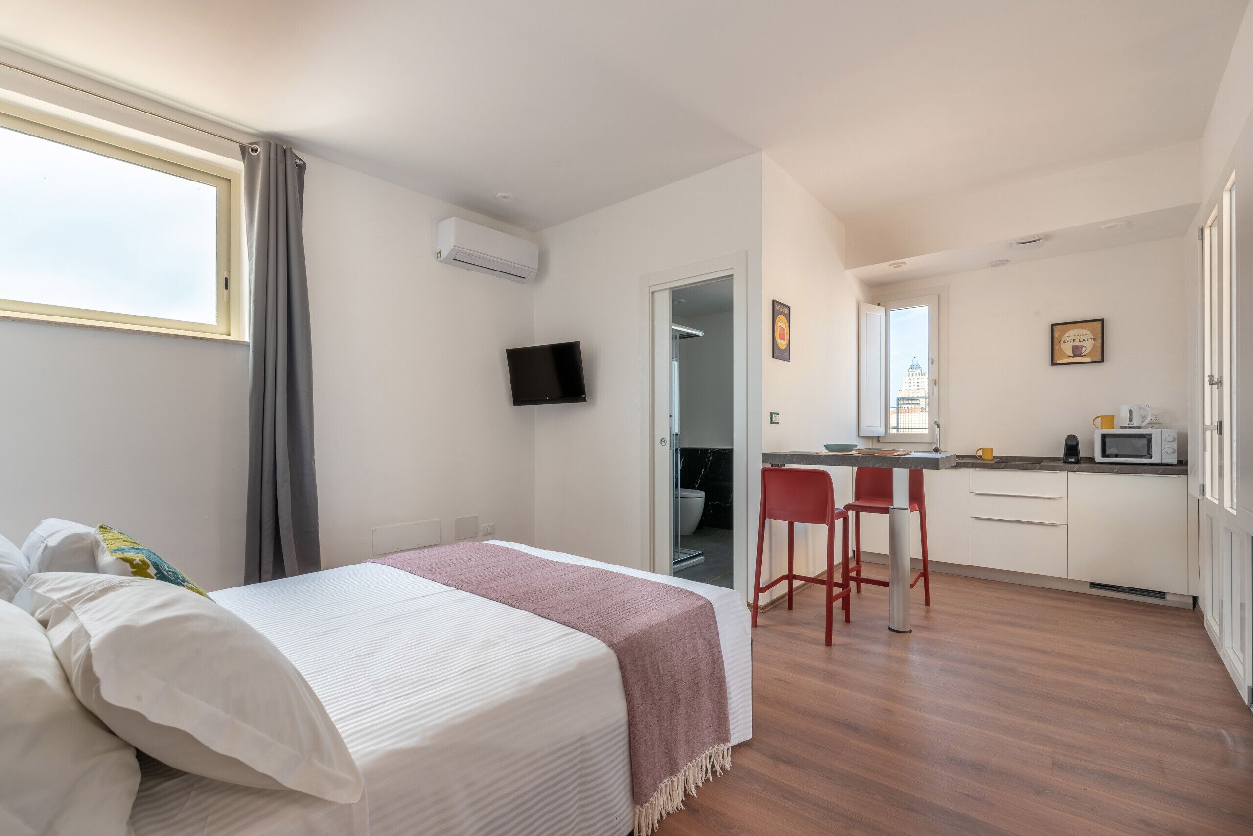 A bedroom with a bed, a TV, and a view of the bathroom.