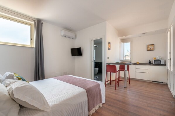 A bedroom with a bed, a TV, and a view of the bathroom.