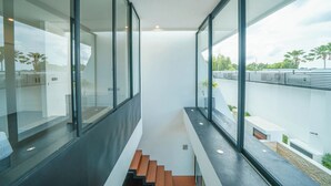 Een modern interieur met grote glasramen, een trap en uitzicht op een brug en groen.