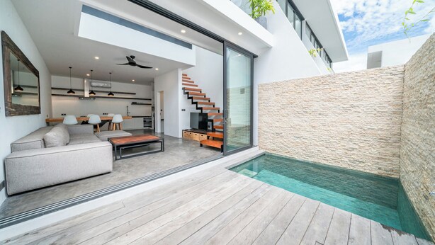 Een modern huis met een houten terras, een overdekt zwembad en een trap naar een tweede verdieping.