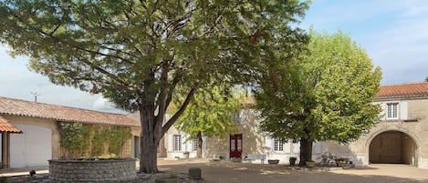 Un patio con un árbol grande, muros de piedra y un edificio con puerta roja.