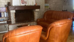 A living room with a fireplace, stone walls, and a brown leather armchair. - Guest Room 'Room 1 for 2 People' with Shared Pool, Shared Terrace and Wi-Fi (Segonzac)