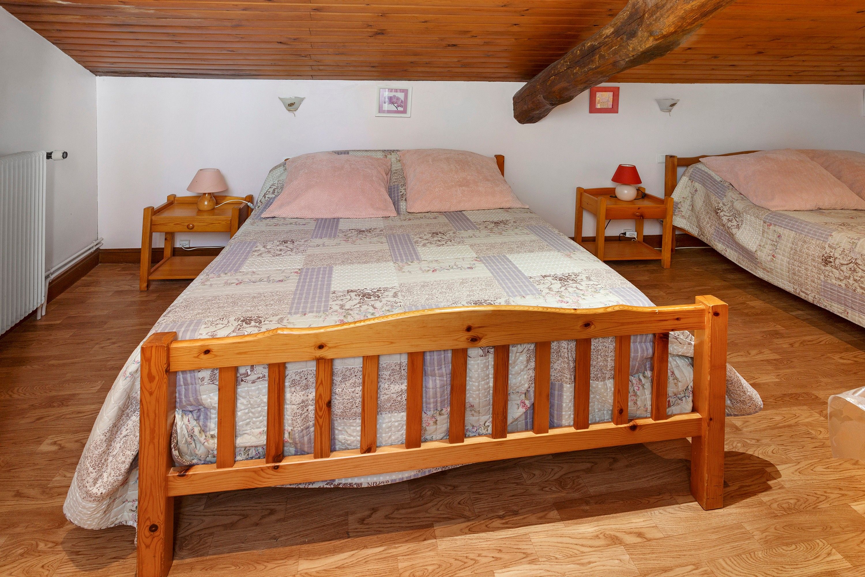 Een slaapkamer met een houten bed, twee nachtkastjes, een radiator en een schuine kap.