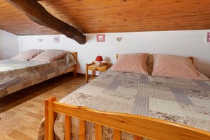 Une chambre avec deux lits simples, un plancher en bois, un plafond en pente et une petite table de chevet avec une lampe.