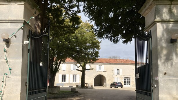 A gated entrance with a stone building, a tree, and a car parked inside. - Guest Room 'Lavande 4 Persons' with Shared Pool, Shared Terrace and Wi-Fi (Segonzac)