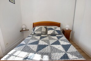 Ein Bett mit einem geometrisch gemusterten Bettbezug, zwei Nachttischlampen und einem Holzkopfstück.