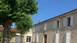 A stone building with white shutters, a red door, and a gravel courtyard with a table and chairs. - Bed and Breakfast 'D'hôtes' with Shared Pool, Shared Terrace and Wi-Fi (Segonzac)