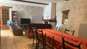 A dining area with a long table, chairs, a sofa, a television, and a bookshelf. - Bed and Breakfast 'D'hôtes' with Shared Pool, Shared Terrace and Wi-Fi (Segonzac)