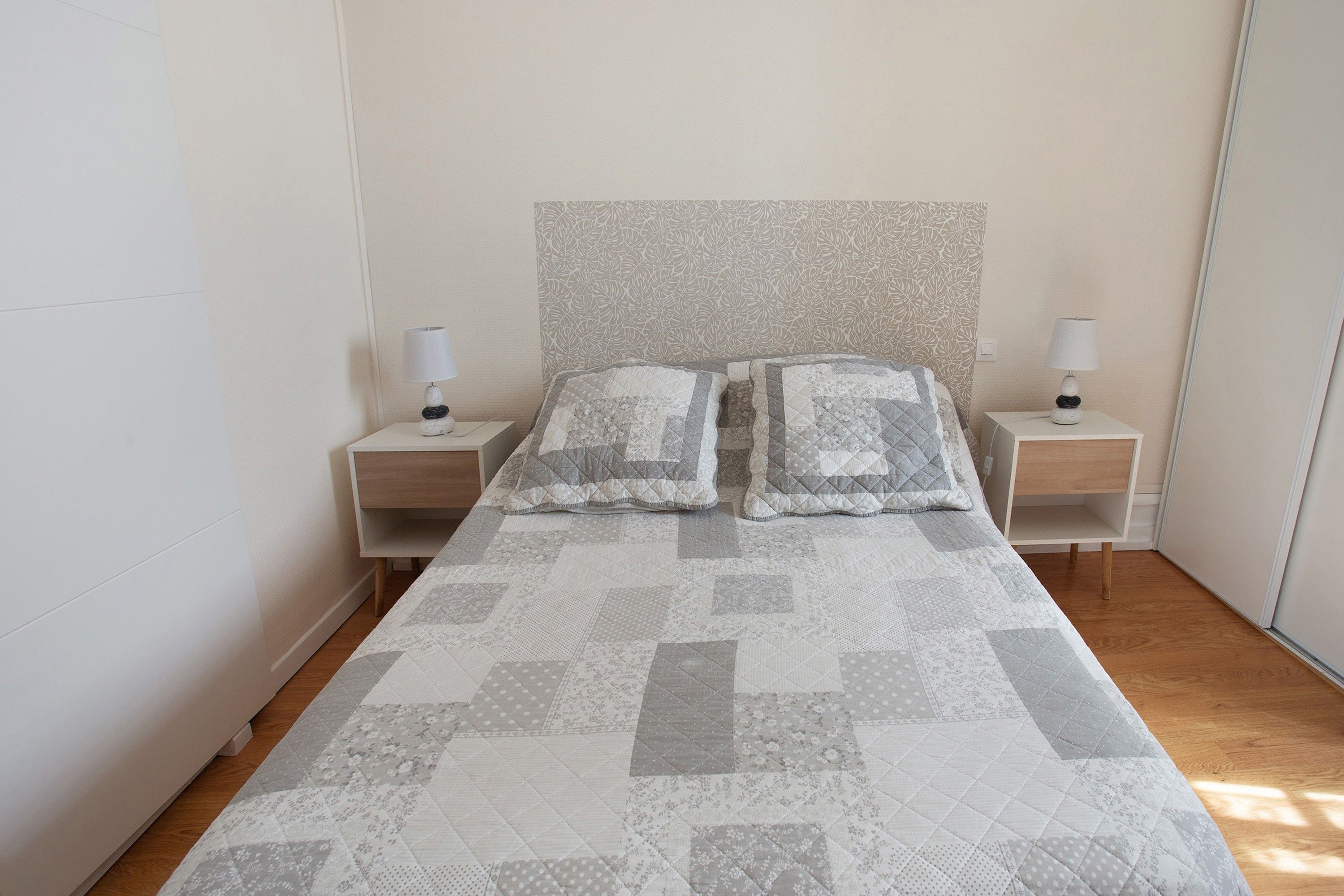 Een bed met een sprei, twee nachtkastjes met lampen, en een hoofdbord met dessin.