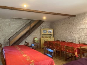 Ein Essbereich mit einem langen Tisch, der rot bedeckt ist und von Holzsesseln umgeben wird. Eine Treppe führt zu einer erhöhten Ebene.