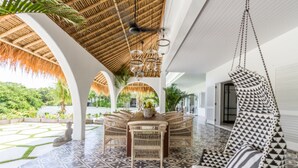 Un espacio interior amplio con techo de paja, muebles de mimbre y suelo estampado.