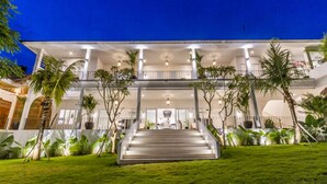 Un edificio de varios pisos con una escalera central, rodeado de exuberante vegetación y palmeras.
