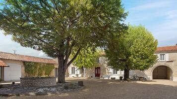 Une cour avec un grand arbre, des murs en pierre et un bâtiment doté d’une porte rouge.