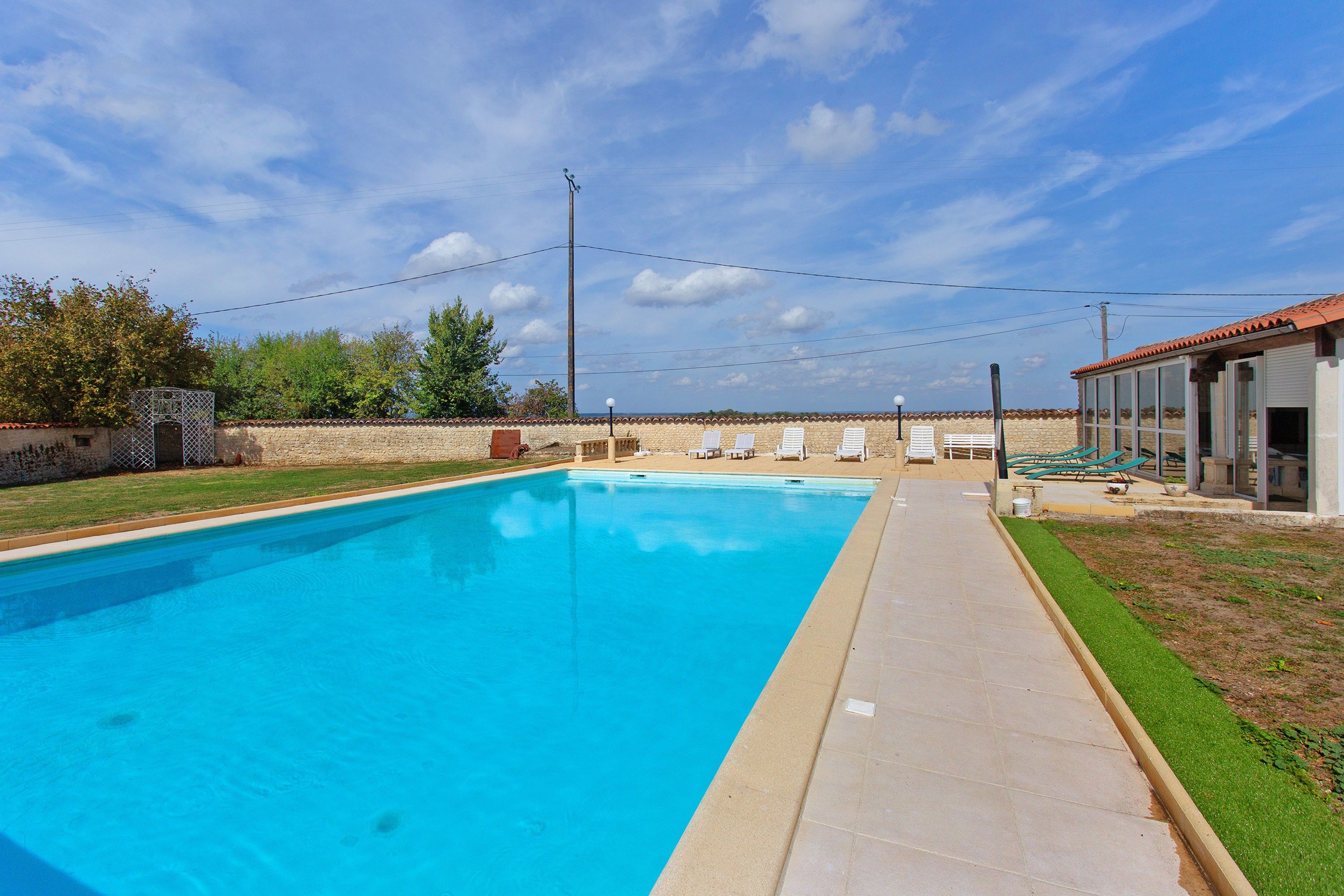 Une piscine à l’eau d’un bleu limpide, entourée d’une terrasse carrelée et d’un mur en pierre.