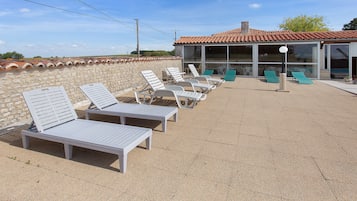 A sunlit outdoor seating area with lounge chairs and a building with a tiled roof.